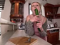 A housewife experiments with a cucumber in the kitchen.